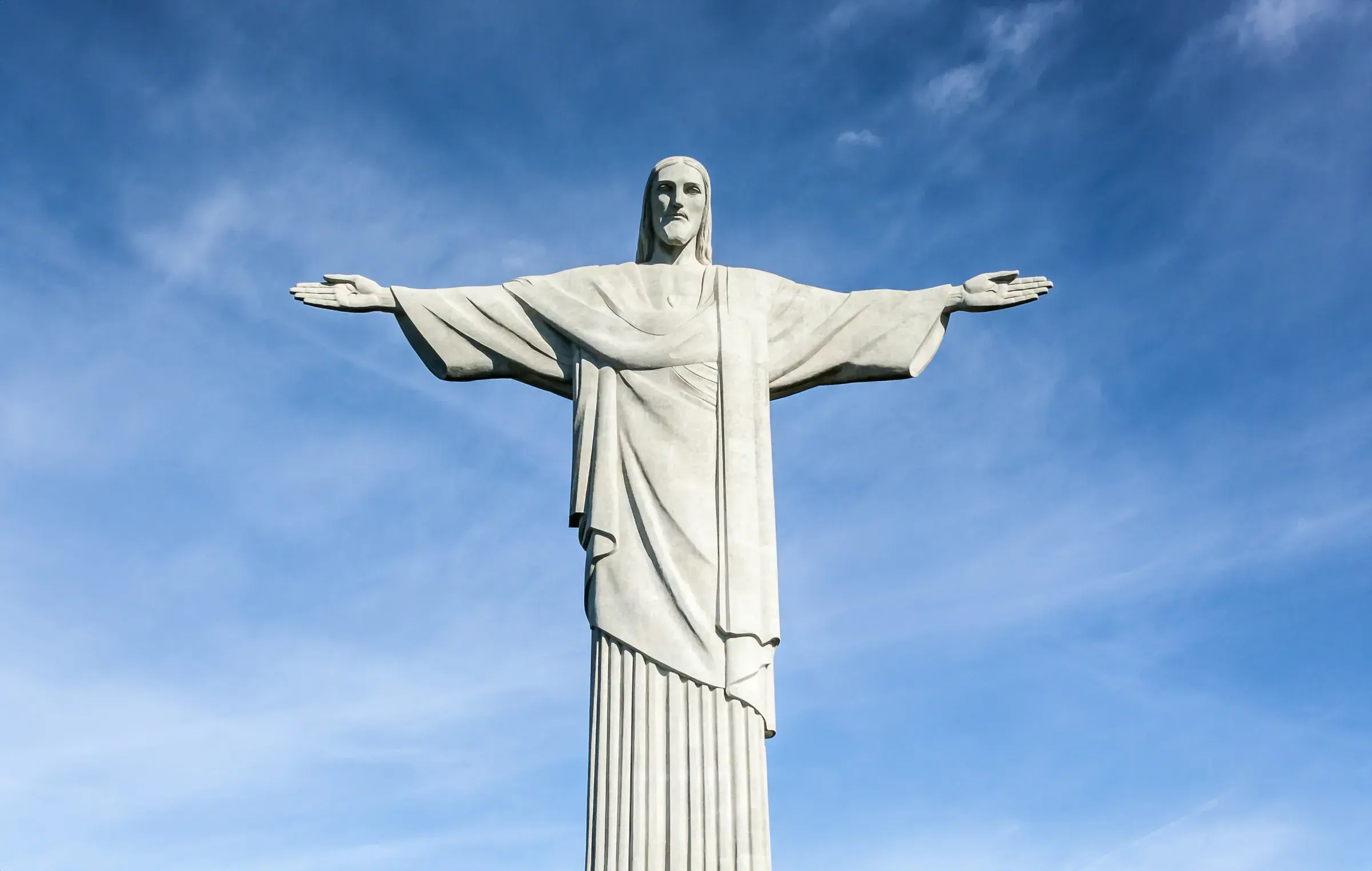 Statue of Christ the Redeemer with outstretched arms against a blue sky with light clouds, in Rio de Janeiro