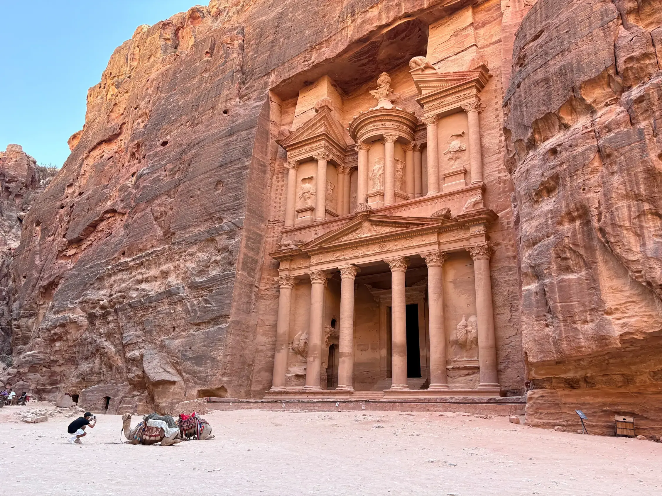 Facade of the Treasury (Al-Khazneh) carved into the rose-colored sandstone of Petra, with camels resting in front